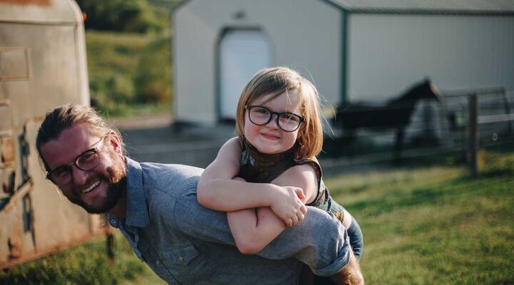 Father With Beard And Long Hair Giving Daughter Piggy Back On Farm
