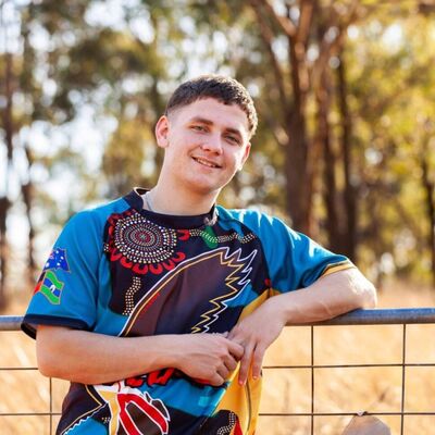 Aboriginal teenagher wearing colourful shirt leaning on fence