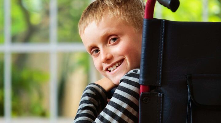 Boy In Wheelchair Looking Over Shoulder Smiling Into Camera