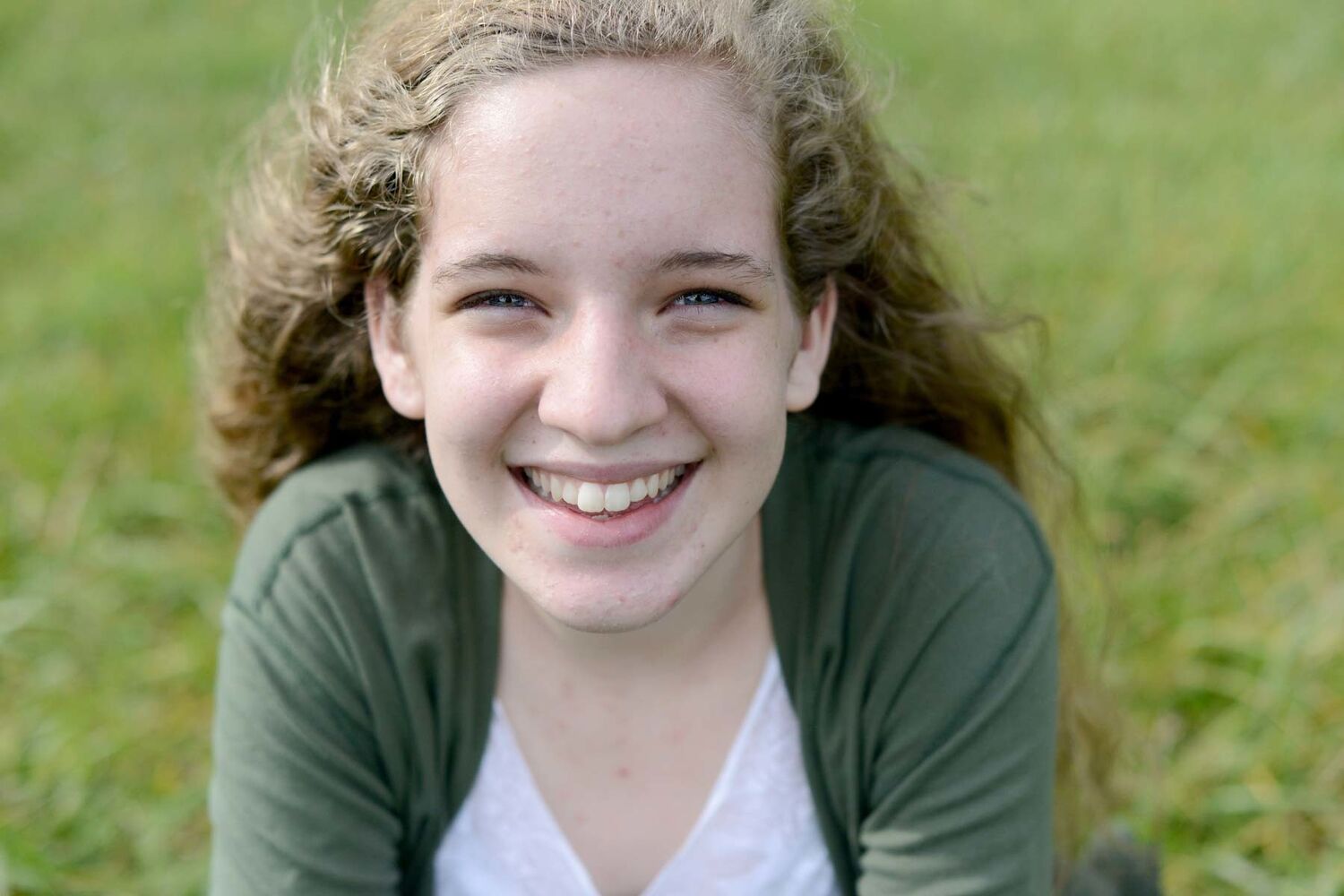Teenage Girl Sitting On Grass Smiling With Wind Blowing Her Hair