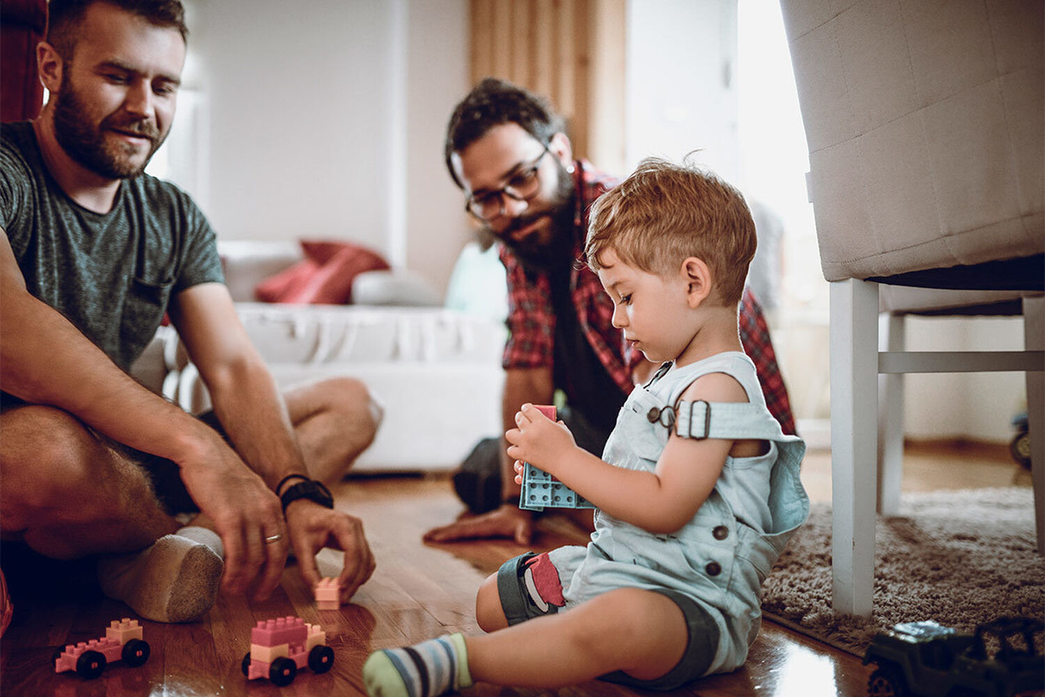 Gay Dads Sitting On Floor With Son Playing With Lego Cars