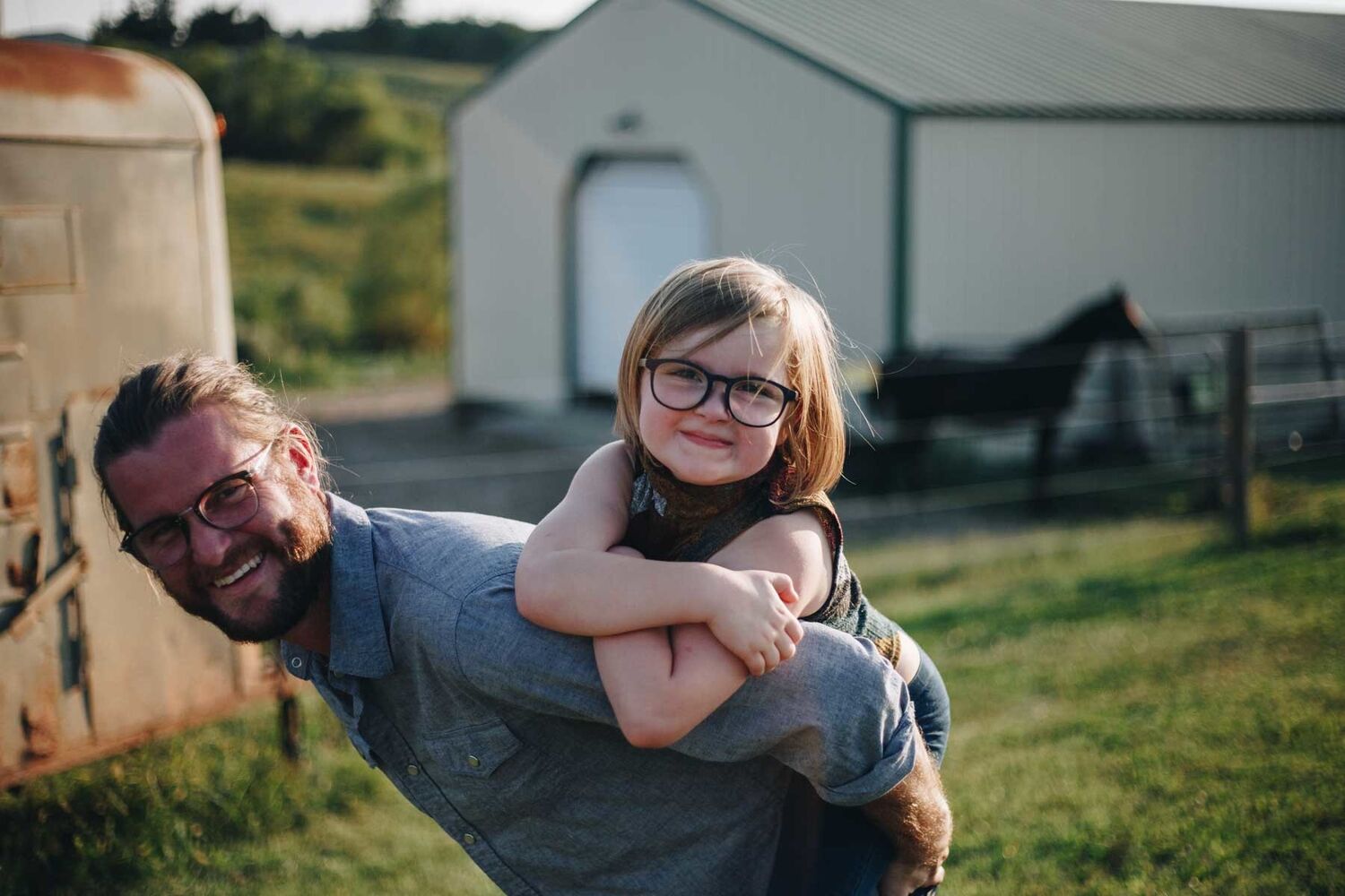 Father With Beard And Long Hair Giving Daughter Piggy Back On Farm