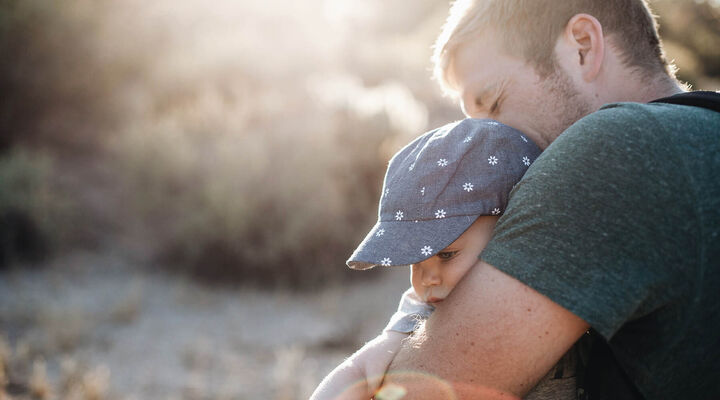 Father Hugging Young Child With A Hat On
