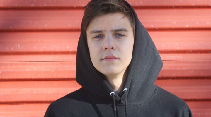 Teen boy in black hoodie standing against red panel wall