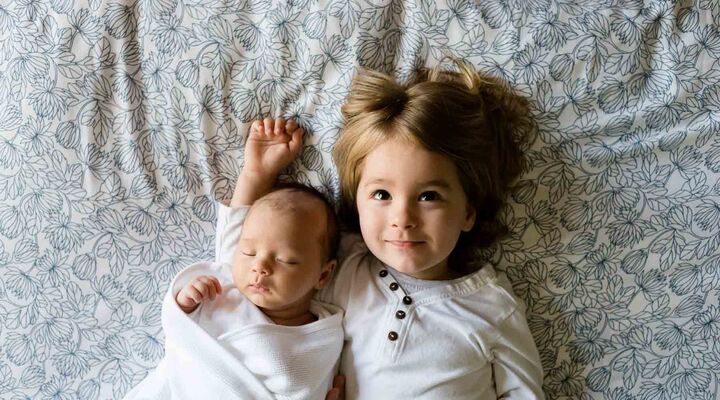 Baby And Toddler Brothers Lying On Bedsheet