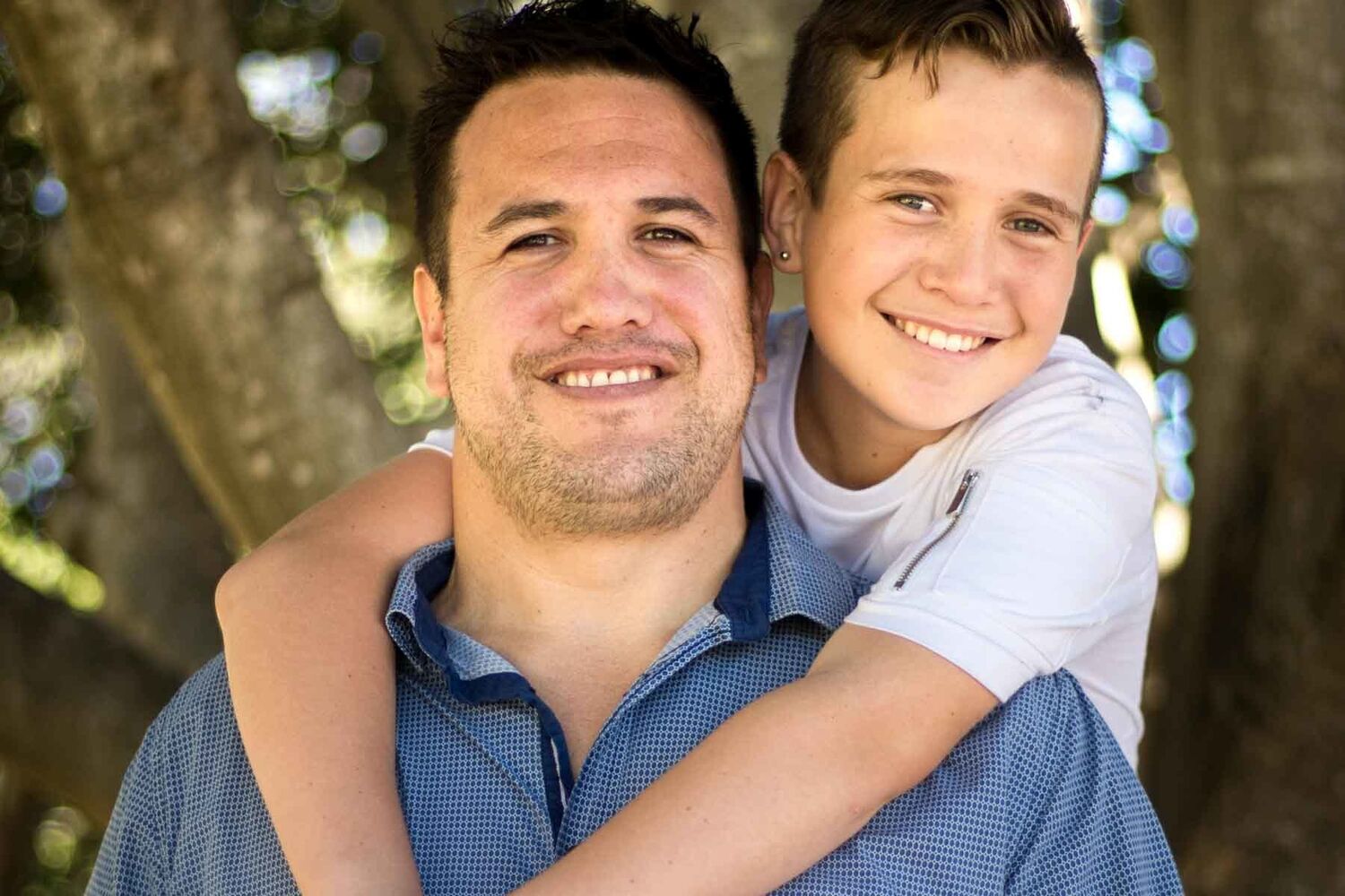 Boy With Arms Around Dads Neck Both Smiling Into Camera