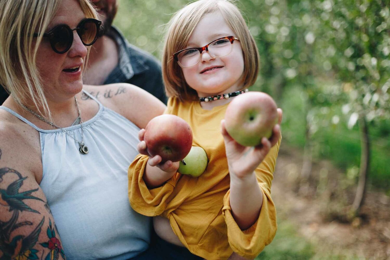 Girl Holding Apples Being Held By Mother In Orchard