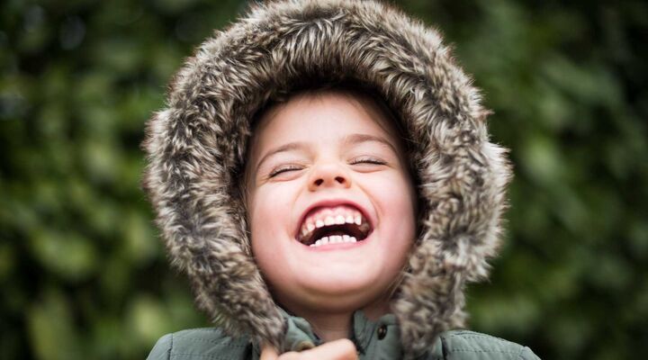 Child Wearing Jacket With Furry Hood Laughing With Eyes Closed