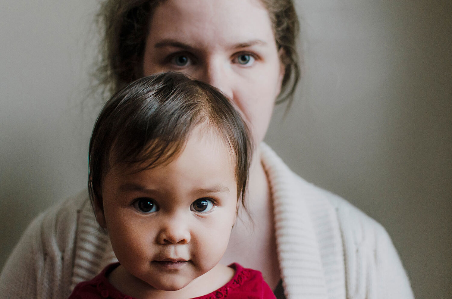 toddler with brown eyes looking into camera with mother behind