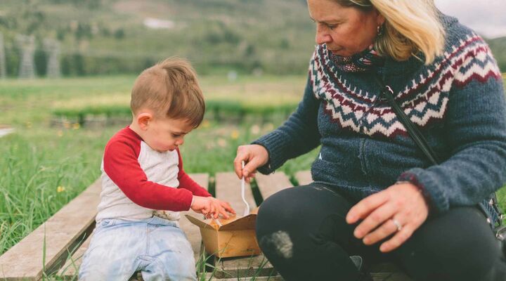 Grandmother And Toddler Sitting On Wooden Crate In Field Eating Take Away