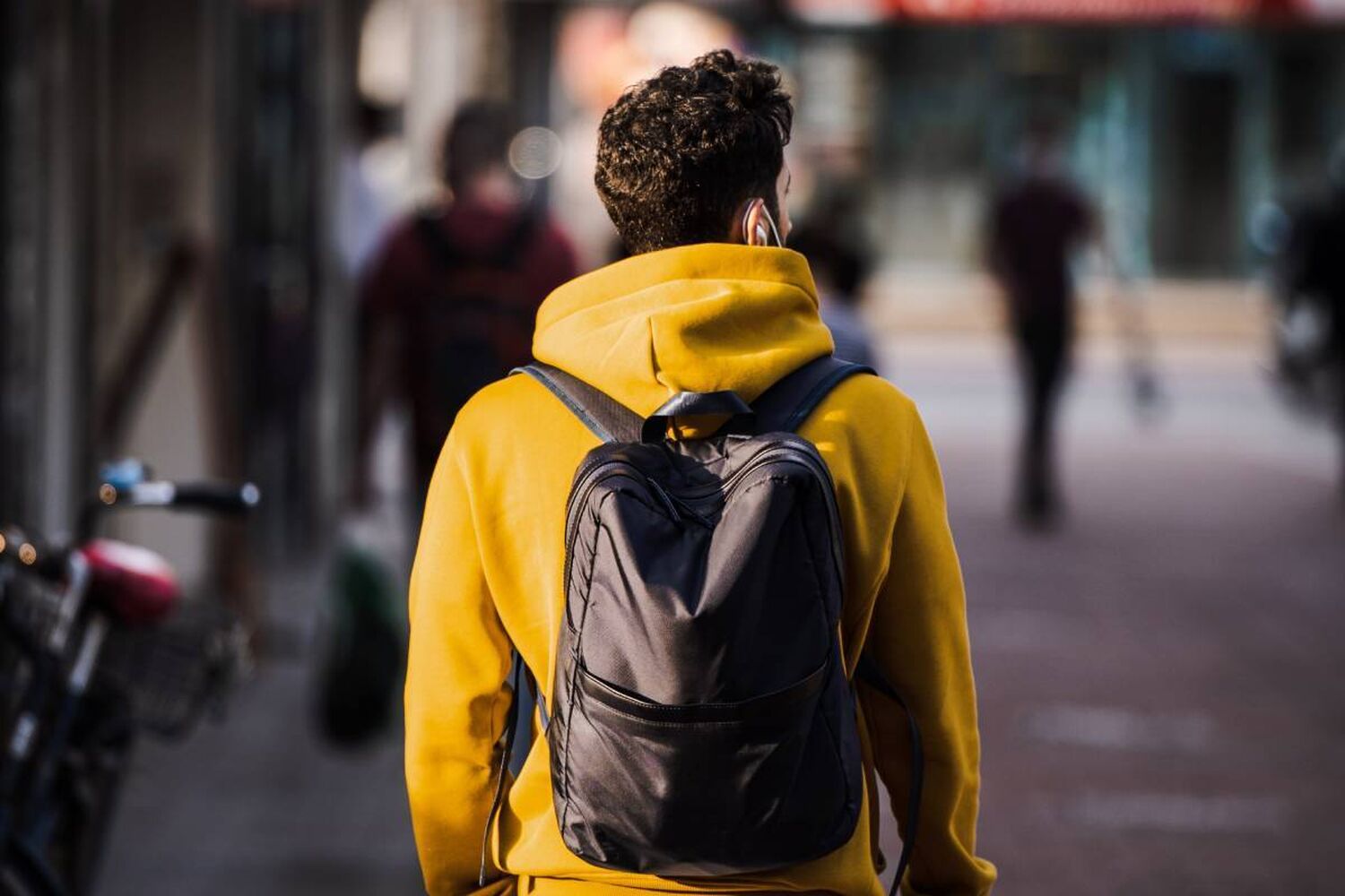 Young Man In Yellow Hoodie With Black Backpack Walking Away