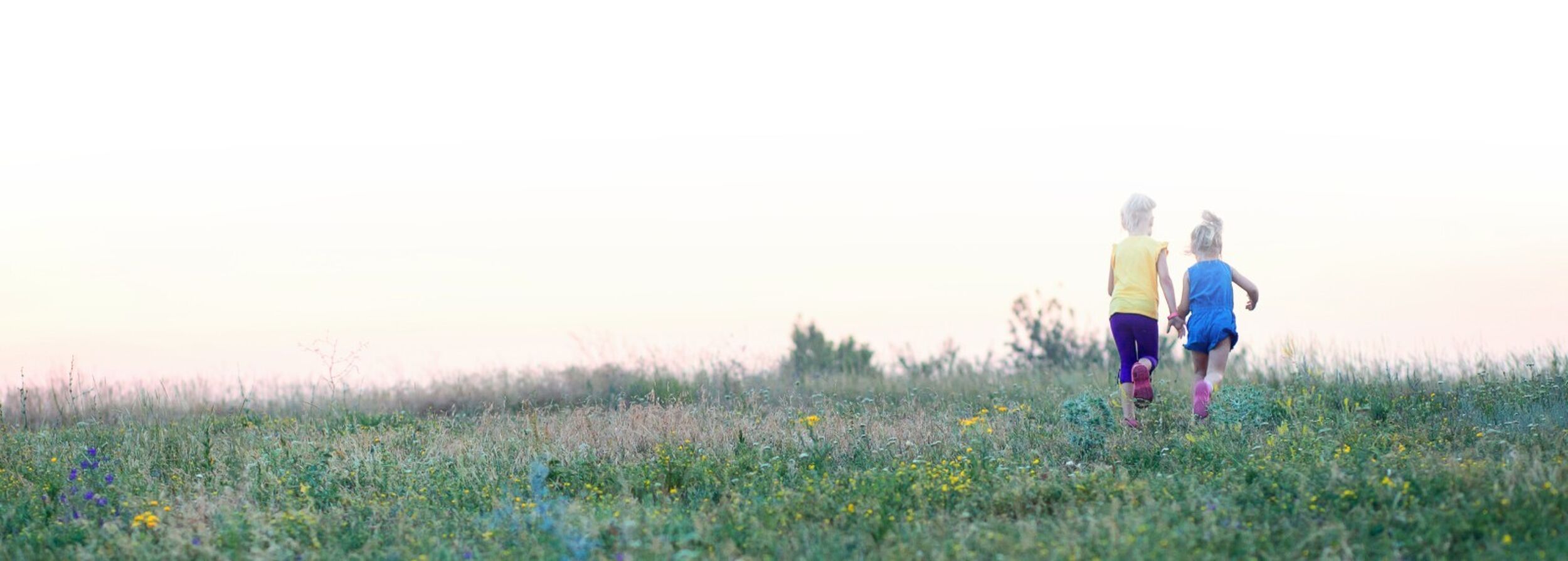 Two girls running in a field whitesky