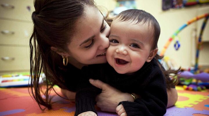 Multicultural Mother And Baby Lying On Coloured Mats In Nursery Smiling