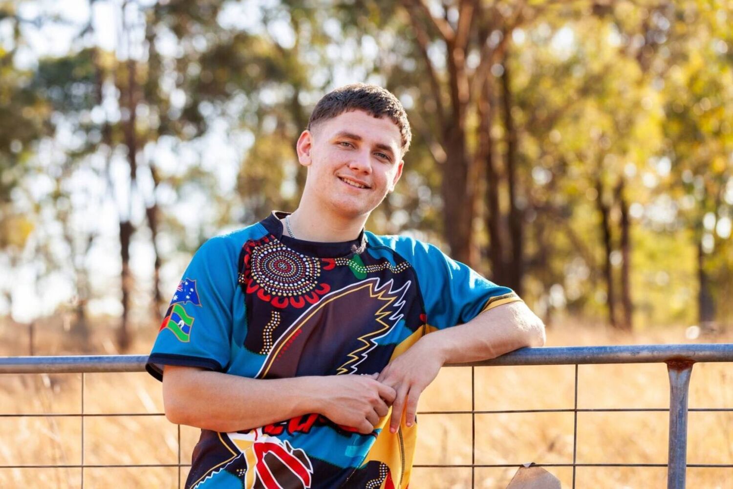 Aboriginal teenagher wearing colourful shirt leaning on fence