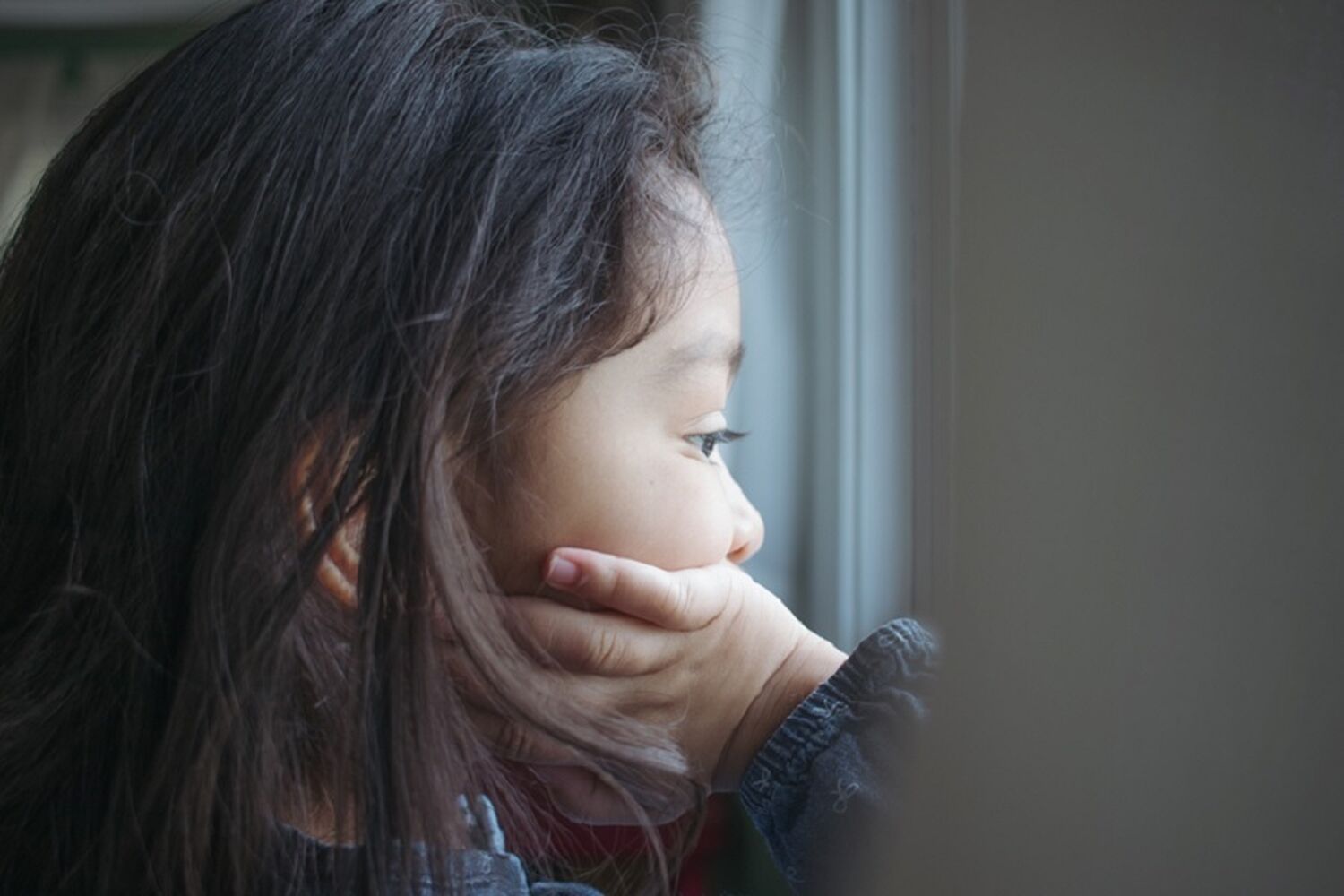 A Toddler Girl Looking Out The Window With Her Hand On Her Face