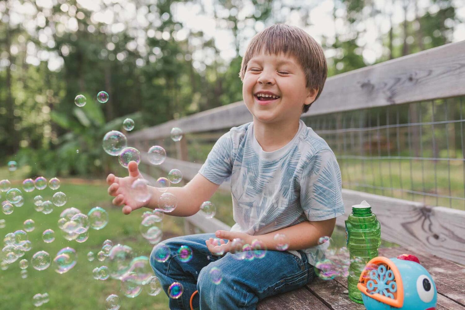 Boy Wearing Jeans And Tshirt Sitting On Bench Outside Playing With Bubbles