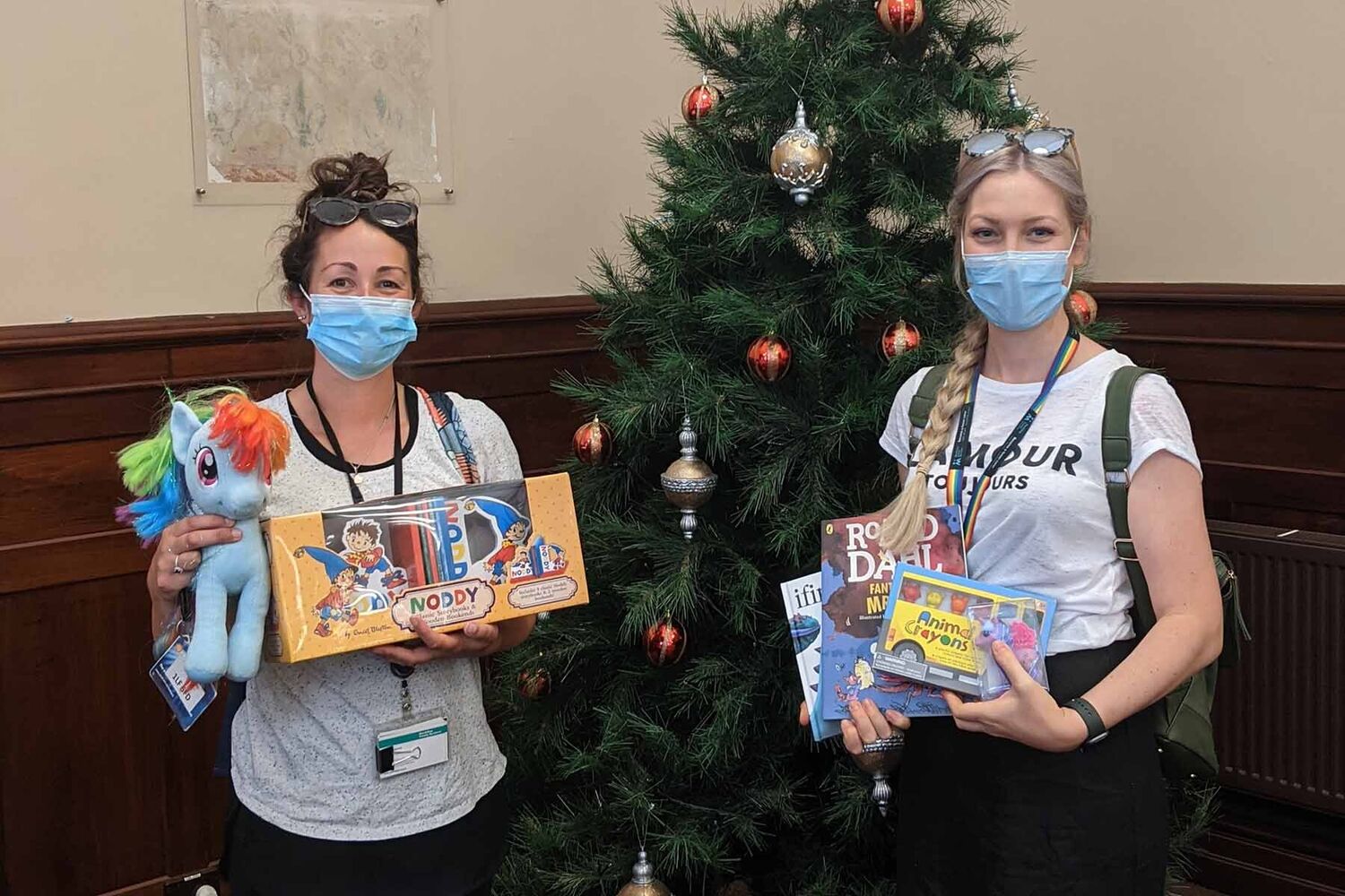 Mackillop Staff Holding Gifts And Toys Infront Of Christmas Tree Wearing Covid Masks