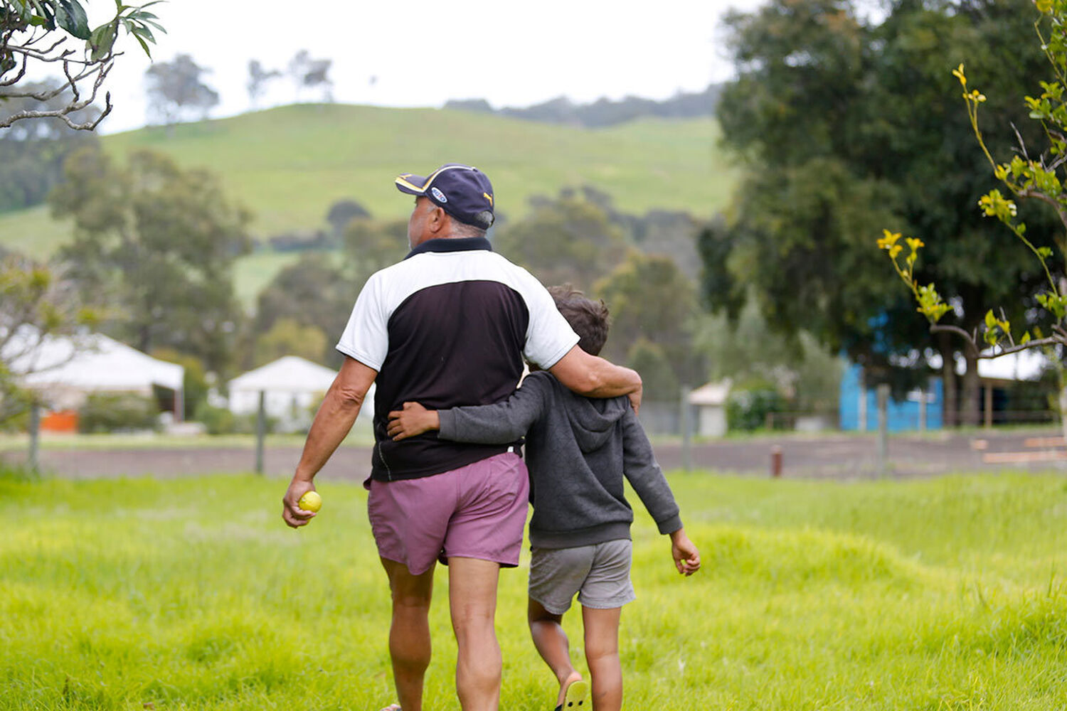 Foster Carer Francis Khan Walking With Arm Around Young Boy Outdoors At Roelands Village