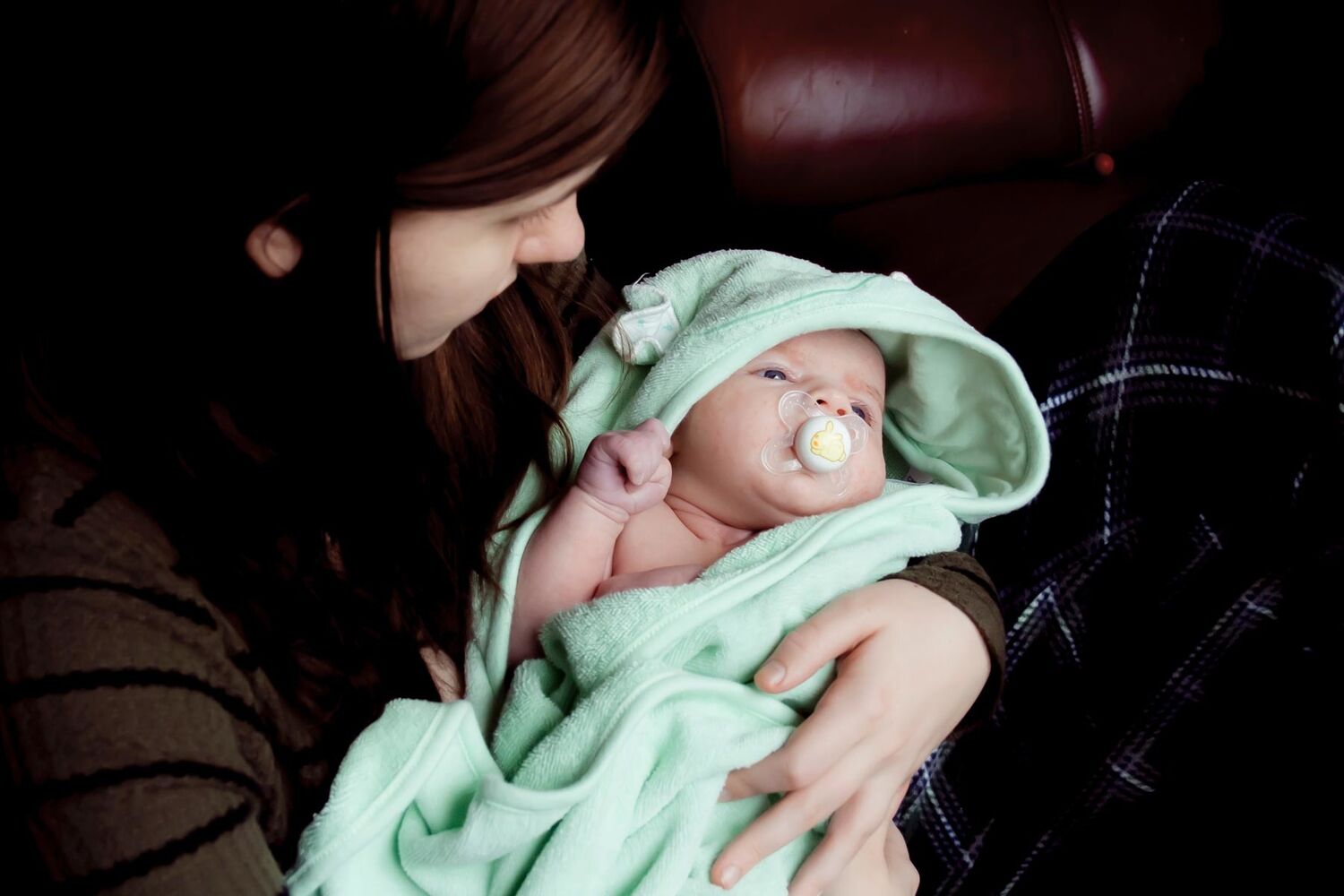 Young Mother Holding Baby In Green Swaddle With Dummy