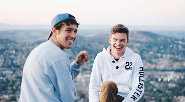 Teenage Boys In Sweatshirts Laughing Sitting In Ledge Above Town In Background