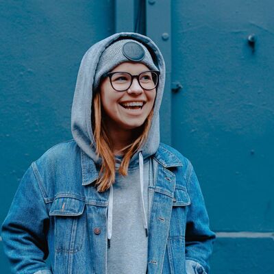 Teenage Girl In Denim Jacket And Hoodie Smiling Standing Against Blue Wall