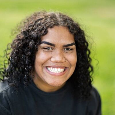 Young Aboriginal Woman With Curly Hair Smiling In Front Of Green Background