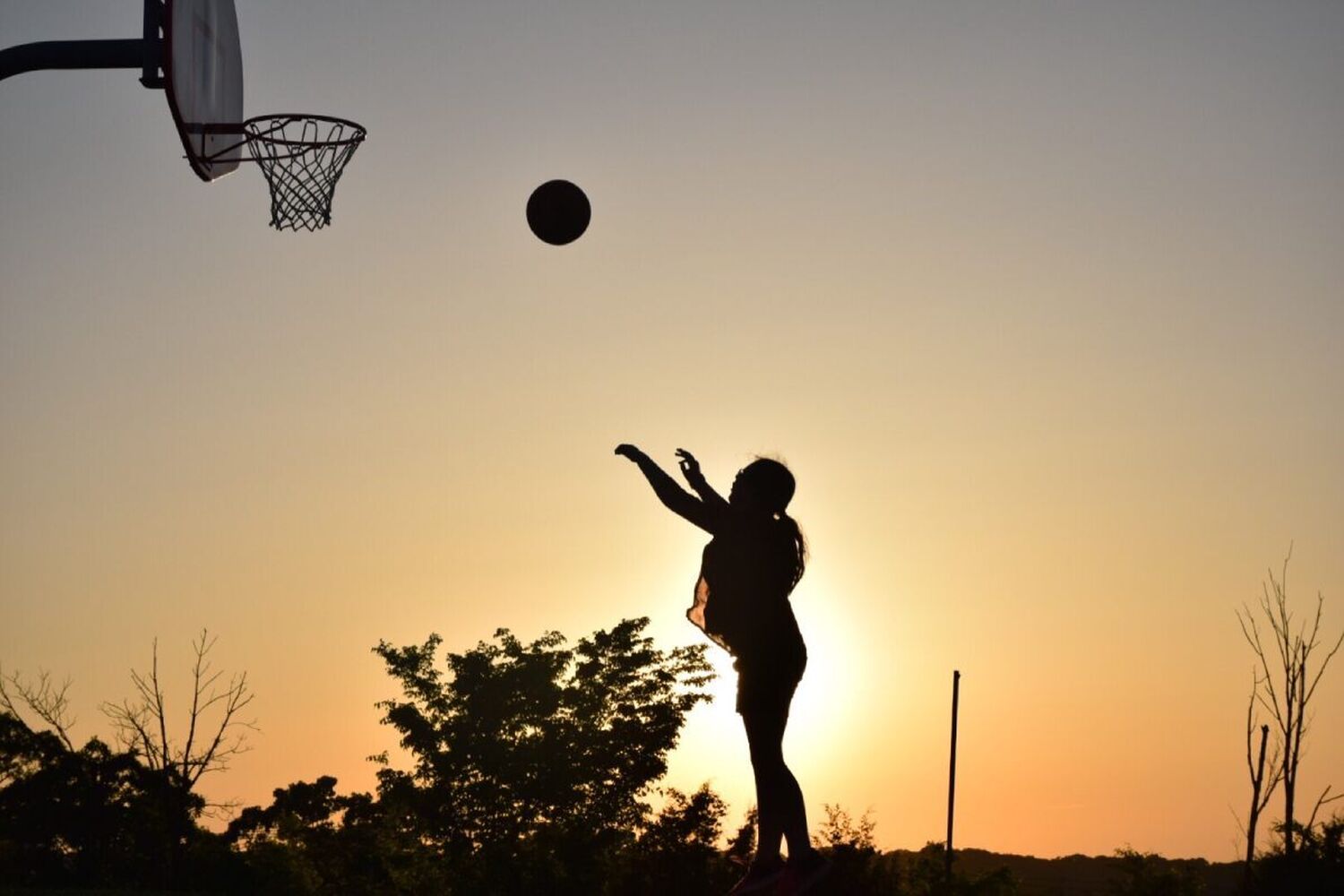 Girl playing basketball at sunset
