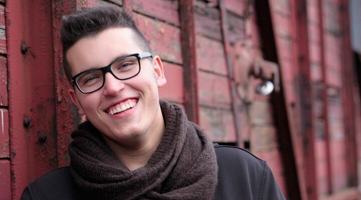 Young Man Wearing Glasses And Scarf Standing In Front Of Red Wall Smiling