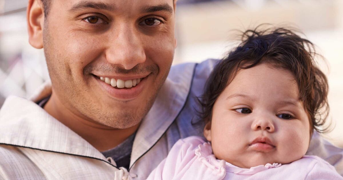 father holding baby girl with chubby cheeks smiling into camera